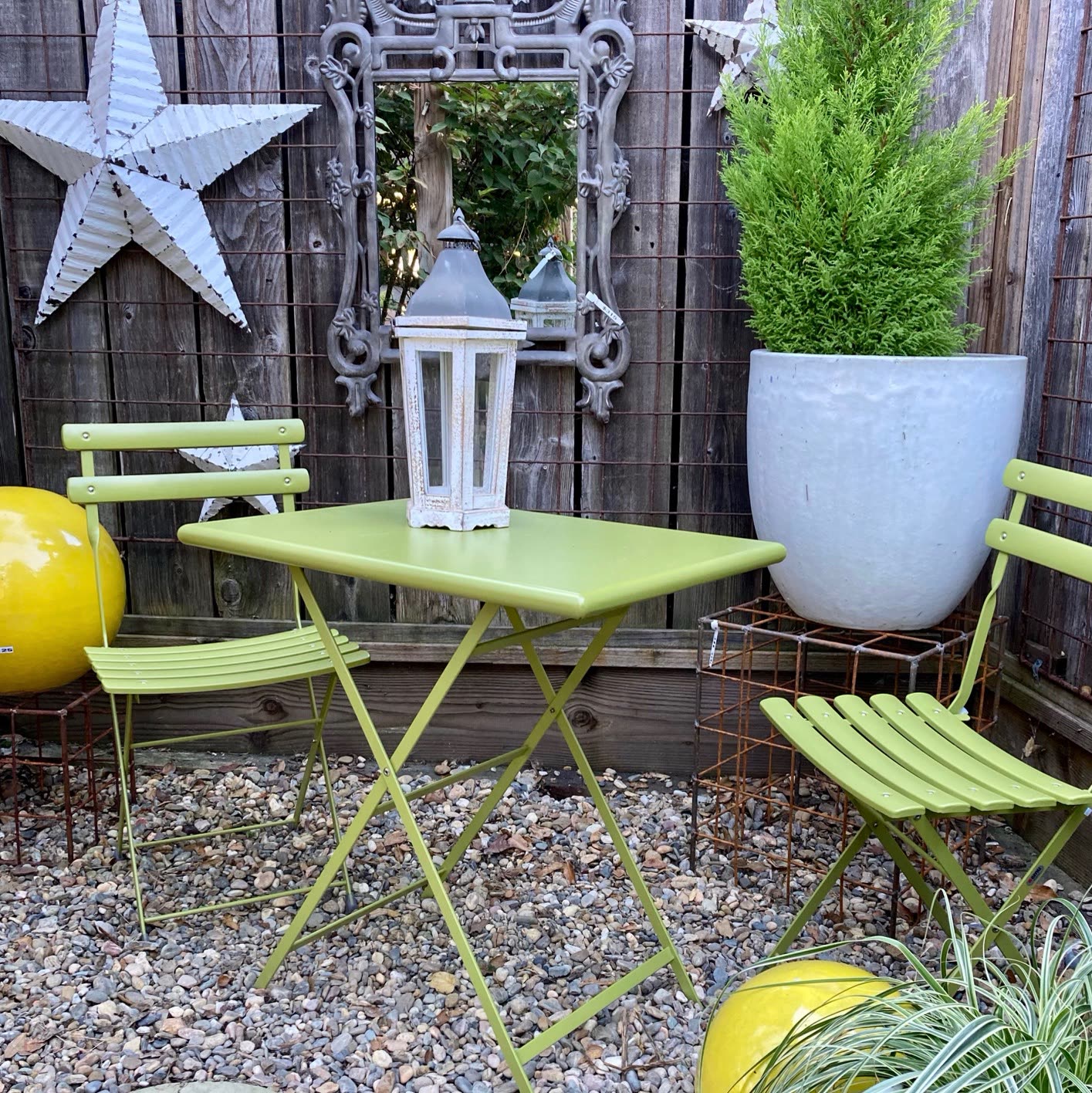 A green bistro table and chairs among pots and garden art